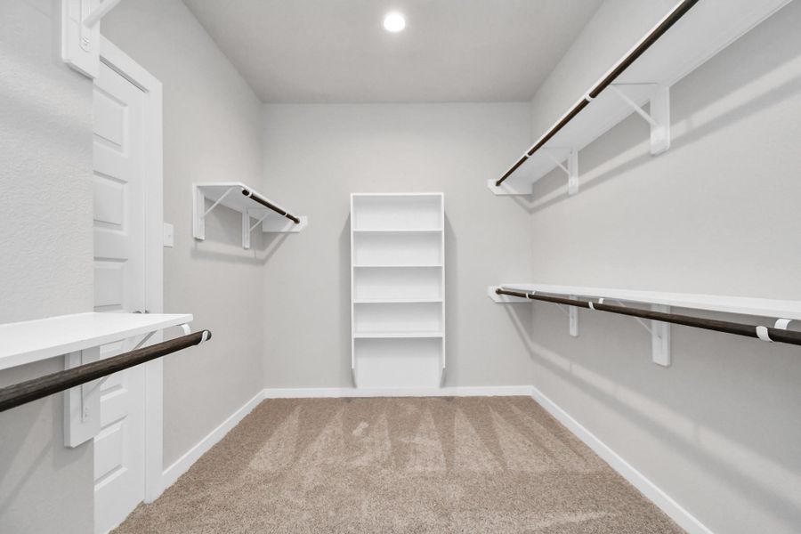 Expansive walk-in closet, adorned with high ceilings, luxurious carpet, and built in shelves. Sample photo of completed home with similar floor plan. Actual colors and selections may vary.