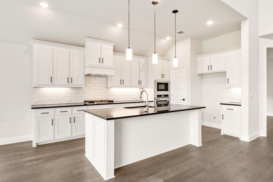 Kitchen with white cabinets, dark countertops, center island, pendant lights, and hardwood floors Kitchen with white cabinets, dark countertops, center island, pendant lights, and hardwood floors