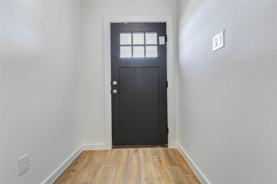 Step inside to a bright entryway featuring a black front door, wood-look tile flooring, and clean white walls. The compact foyer feels fresh and functional, offering a crisp first impression with natural light from the door’s window panels and a neutral design ready for personal touches. Step inside to a bright entryway featuring a black front door, wood-look tile flooring, and clean white walls. The compact foyer feels fresh and functional, offering a crisp first impression with natural light from the door’s window panels and a neutral design ready for personal touches.