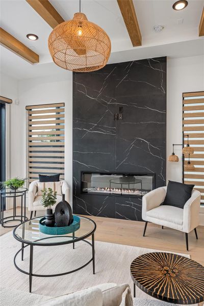 An elegant electric fireplace framed in porcelain, paired with custom chandeliers and beam detailing, becomes the visual anchor of the space