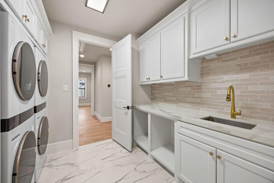 Laundry Room is equipped w/ TWO SETS of full size stackable Washer & Dryer included with the home. Double Hamper cubbies built into the counter space w/ sink.