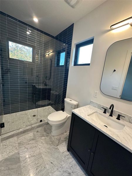 Contemporary bathroom featuring a spacious glass-enclosed shower with dark subway tile, a dark wood-finish vanity with a white countertop and integrated sink, and black hardware