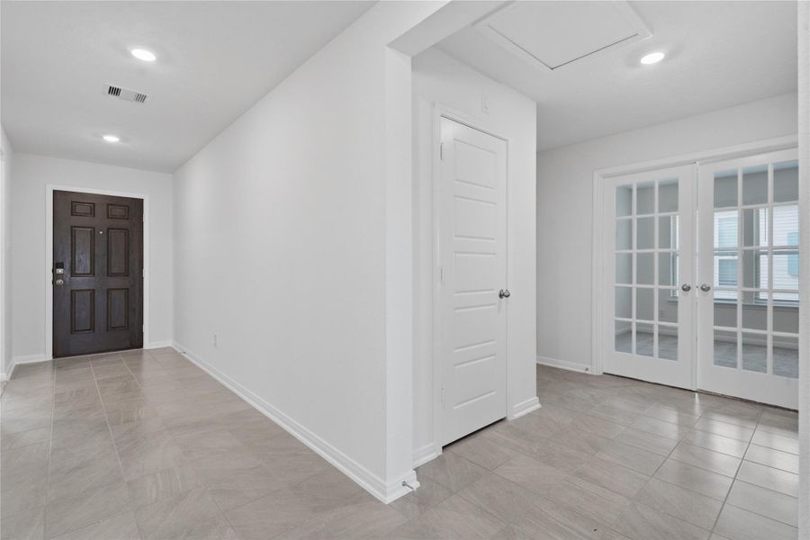 The functional main hallway transitions seamlessly into a private wing, leading back to a secluded den or home office space. This central artery features tile flooring, crisp white trim, and bright recessed lighting that illuminates the path to both the living areas and the Den.