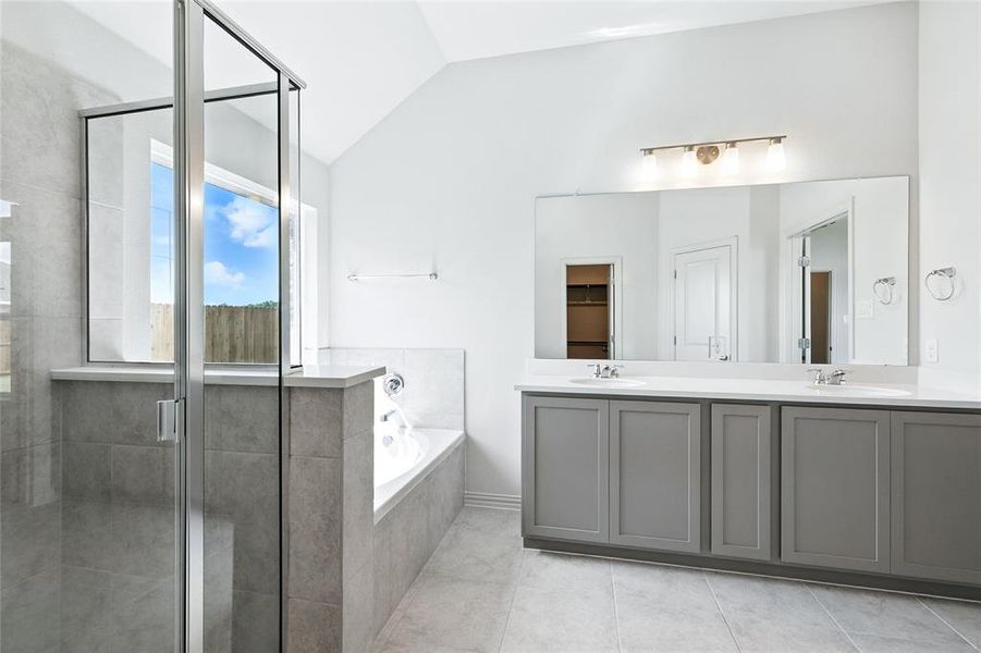 Full bathroom with a shower stall, lofted ceiling, double vanity, a garden tub, and a closet Full bathroom with a shower stall, lofted ceiling, double vanity, a garden tub, and a closet