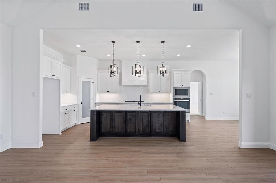 Kitchen featuring arched walkways, an island with sink, light wood-style flooring, a chandelier, and dual tone cabinetry
