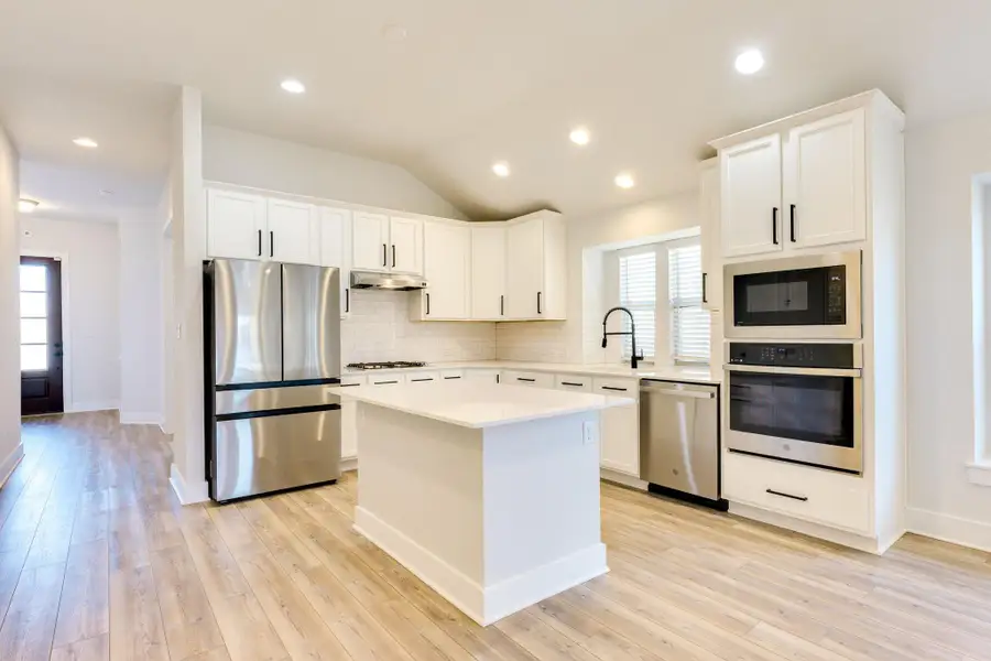 Kitchen featuring appliances with stainless steel finishes, white cabinets, vaulted ceiling, a center island, and decorative backsplash