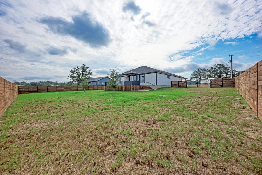 An expansive backyard features a wooden privacy fence and a rear porch under open skies. An expansive backyard features a wooden privacy fence and a rear porch under open skies.