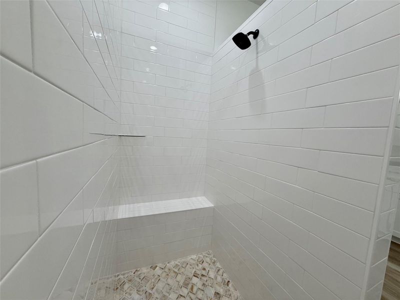 Walk-in shower featuring white subway tile walls, a built-in bench, and a matte black shower head