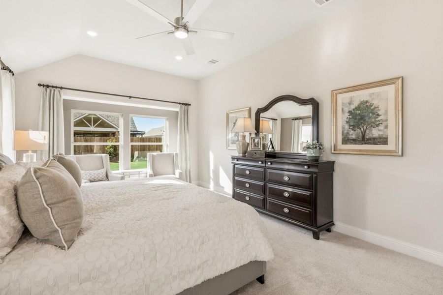 Bedroom with vaulted ceiling, ceiling fan, dark wood dresser, and large window with backyard view Bedroom with vaulted ceiling, ceiling fan, dark wood dresser, and large window with backyard view