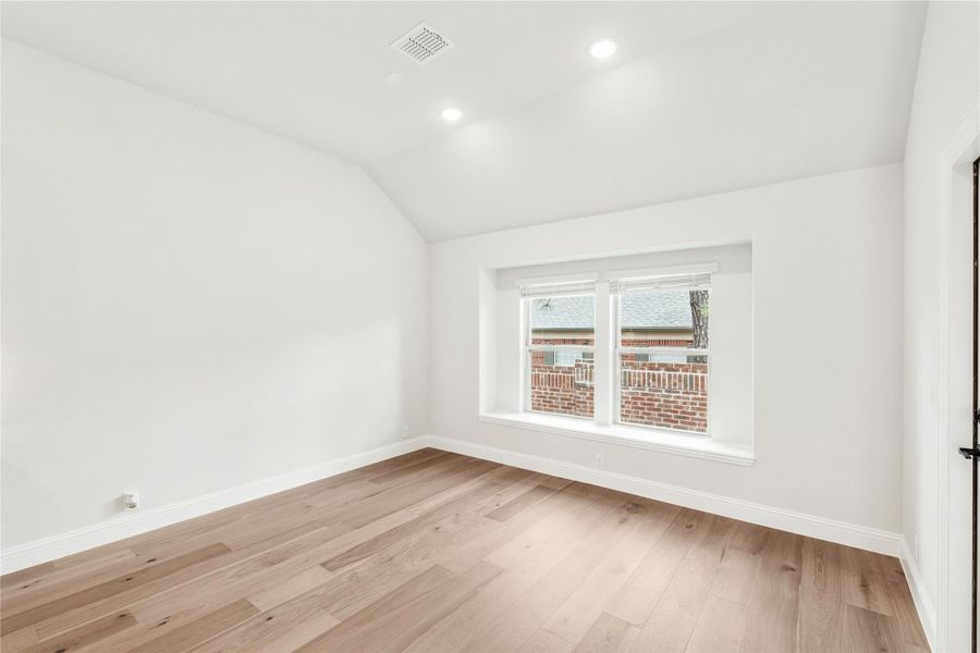 Empty bedroom with vaulted ceiling, light hardwood floors, and a double window with neighborhood view