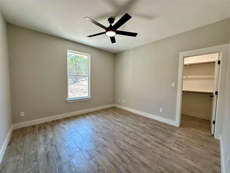 Unfurnished bedroom featuring wood finished floors, a walk in closet, baseboards, and a ceiling fan Unfurnished bedroom featuring wood finished floors, a walk in closet, baseboards, and a ceiling fan