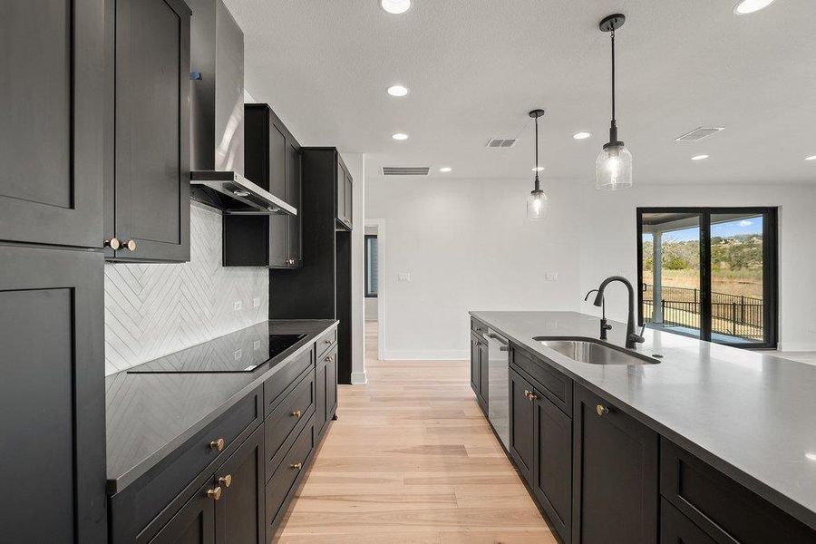 Kitchen with dark cabinets, light wood-style floors, hanging light fixtures, wall chimney exhaust hood, and recessed lighting