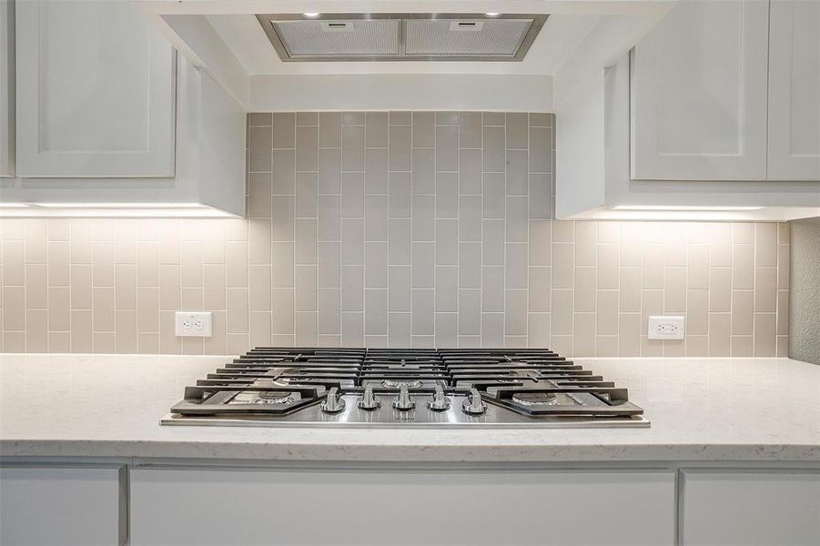 Kitchen with white cabinets, tasteful backsplash, stainless steel gas stovetop, and light stone countertops