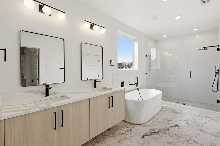 Bathroom featuring a double vanity with light wood cabinetry, a freestanding bathtub, and a glass-enclosed shower