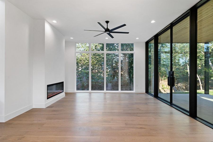 Unfurnished living room featuring floor to ceiling windows, recessed lighting, light wood-type flooring, a glass covered fireplace, and a ceiling fan