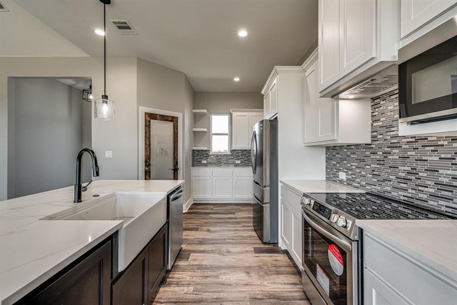 Kitchen featuring light stone counters, stainless steel appliances, hanging light fixtures, and white cabinetry