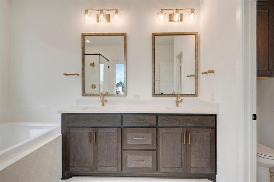 Dual vanity featuring dark wood-finish cabinetry, white countertops, and gold-finish hardware