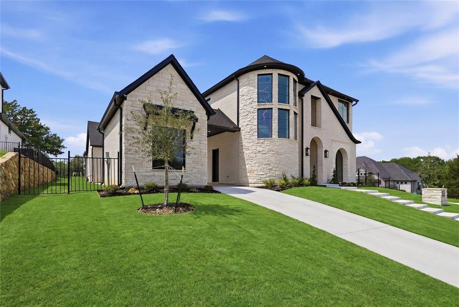 Contemporary stone exterior featuring a circular turret with tall windows, a prominent arched entry, a concrete driveway, and manicured landscaping