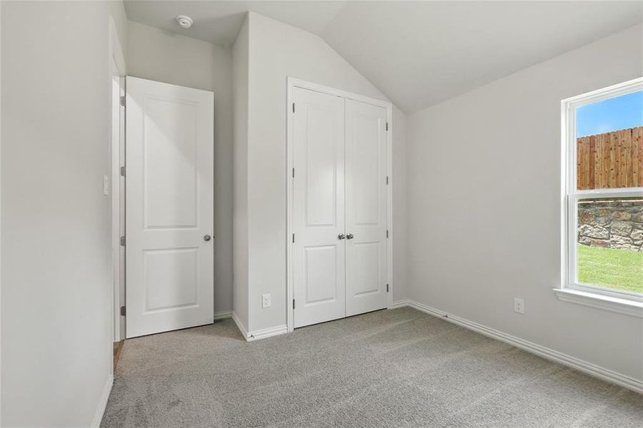 Unfurnished bedroom featuring light colored carpet, vaulted ceiling, and a closet