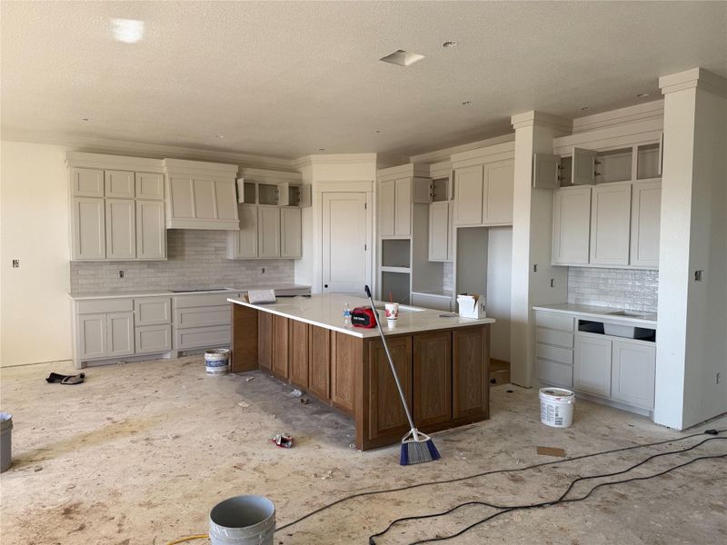Two tone kitchen featuring a center island with sink, two tone cabinets, a kitchen breakfast bar, and tasteful backsplash
