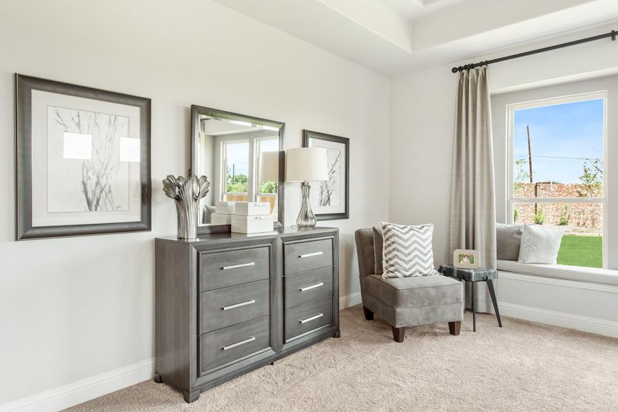 Bedroom sitting area with gray dresser, accent chair, window seat, and tray ceiling Bedroom sitting area with gray dresser, accent chair, window seat, and tray ceiling