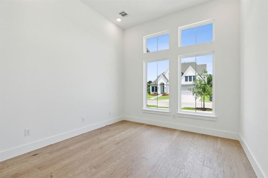 Room featuring high ceilings, recessed lighting, wood-finish flooring, and white baseboards Room featuring high ceilings, recessed lighting, wood-finish flooring, and white baseboards