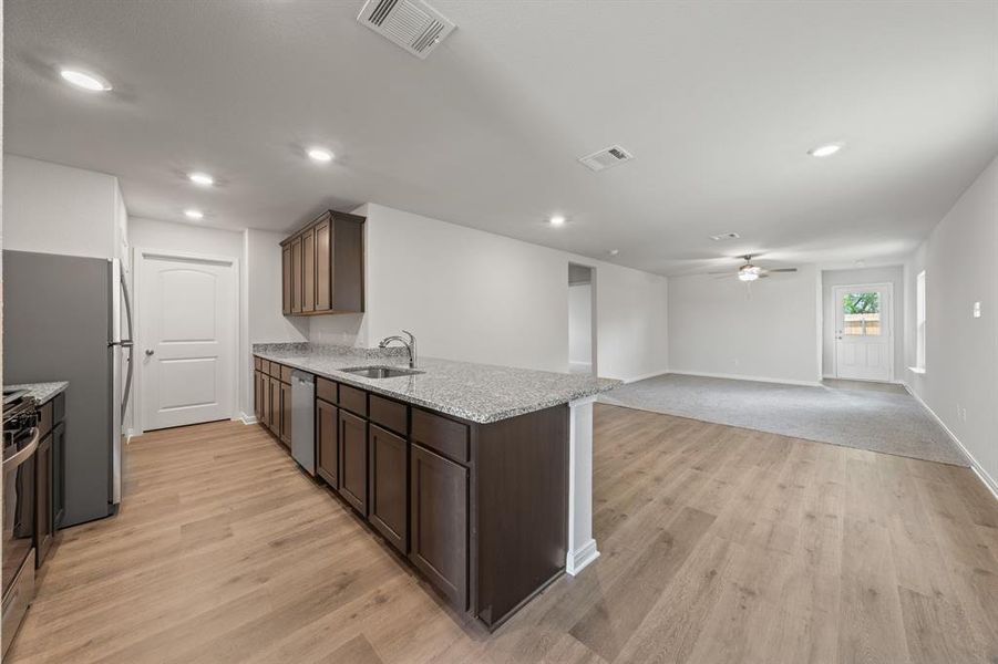 Kitchen with appliances with stainless steel finishes, light stone counters, ceiling fan, sink, and light colored carpet