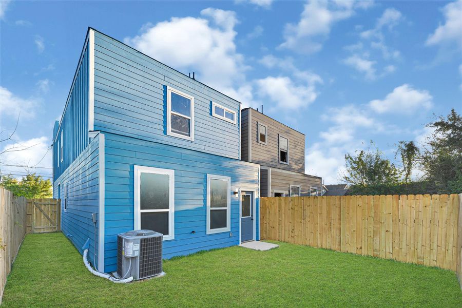 A modern two-story home with vibrant blue siding, featuring a spacious fenced backyard with green grass. The exterior includes large windows and an efficient air conditioning unit, making it ideal for family living.