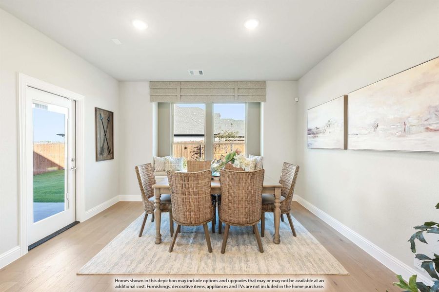 Dining room with round wood table, wicker chairs, light hardwood floors, and glass door to backyard