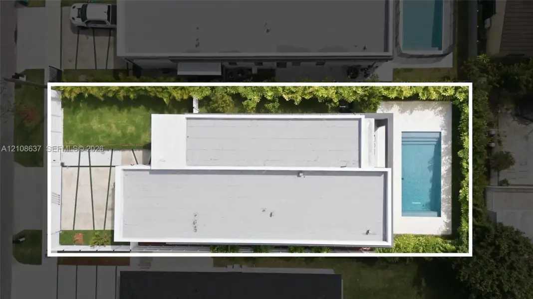 Aerial perspective of property exterior featuring a swimming pool, concrete hardscaping with grass inlays, and perimeter privacy hedging