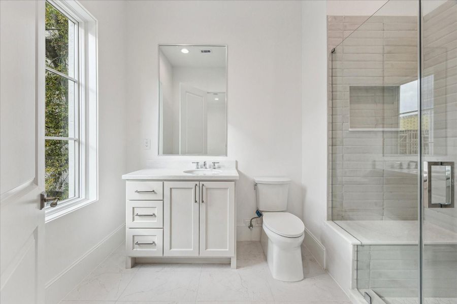 En-suite bath features glassenclosed freestanding shower linedwith Maniscalco Contour glossy tiles,Quartz countertops, and large vanityarea with under-cabinet storage.