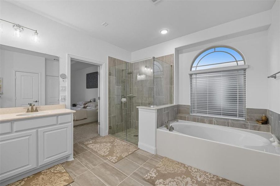 Full bathroom with ensuite bath, a garden tub, a shower stall, vanity, and light tile patterned floors Full bathroom with ensuite bath, a garden tub, a shower stall, vanity, and light tile patterned floors