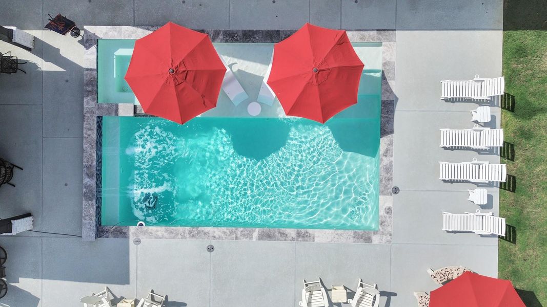 Enjoy a refreshing escape in this stunning backyard oasis featuring a sparkling pool with vibrant red umbrellas and ample lounging space on sleek poolside chairs.