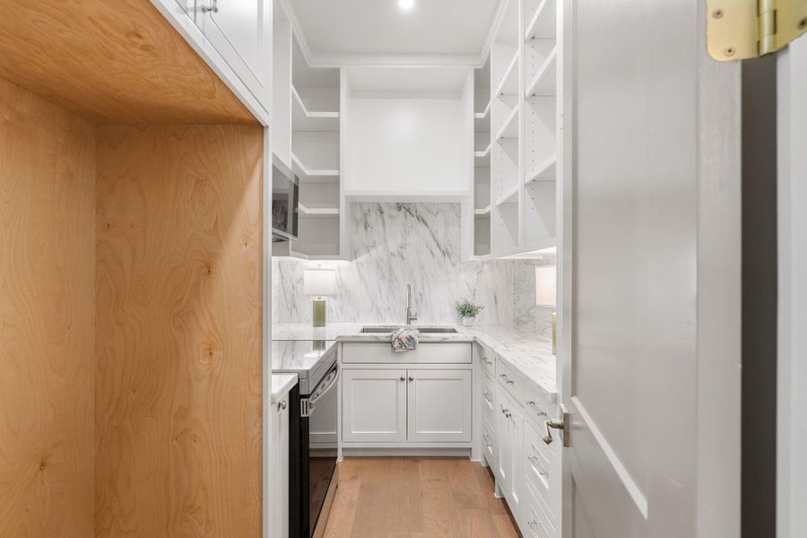 Well-appointed scullery kitchen and walk-in pantry designed for both prep and storage. Full-height marble backsplash and matching countertops create a clean, seamless look, while abundant cabinetry and open shelving provide organized space for everything. Built-in drawers and cabinet storage, a secondary sink, and an additional refrigerator add convenience and function, keeping the main kitchen streamlined and ready for entertaining.