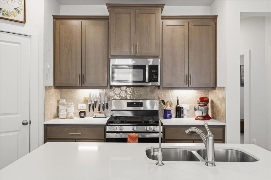 Kitchen with stainless steel appliances, tasteful backsplash, and light stone counters