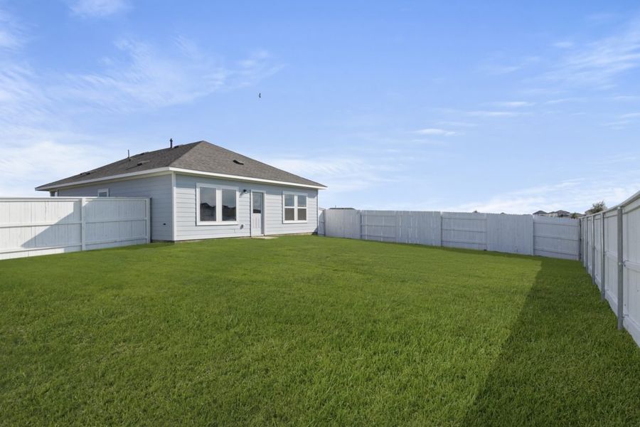 Image of back exterior of a blue one story house with a green grass backyard and a white fence