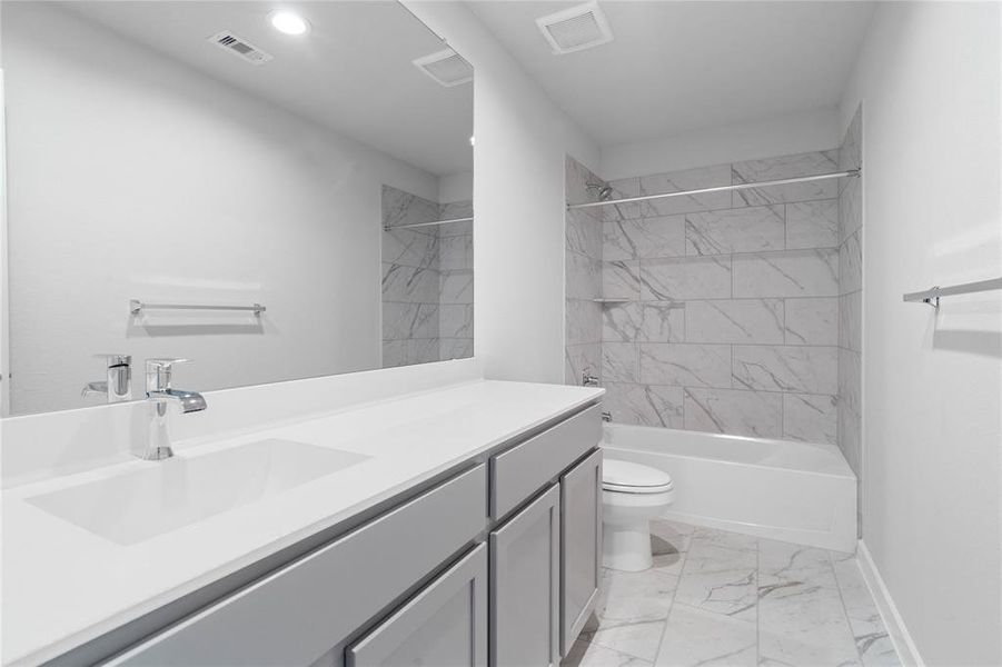 Secondary bath features tile flooring, bath/shower combo with tile surround, stained wood cabinets, beautiful light countertops, mirror, sleek fixtures and modern finishes.