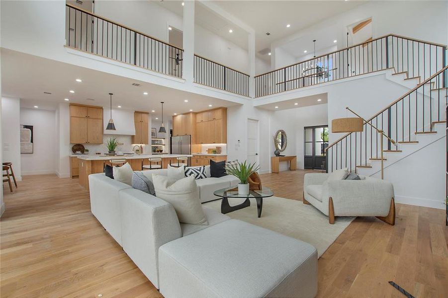 Living area with a towering ceiling, stairway, light wood-style flooring, baseboards, and recessed lighting Living area with a towering ceiling, stairway, light wood-style flooring, baseboards, and recessed lighting