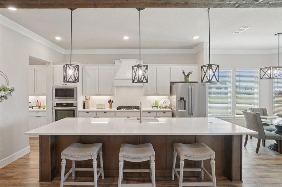 Kitchen featuring crown molding, light wood-look ceramic tile flooring, appliances with stainless steel finishes, a large island with sink, and white cabinets