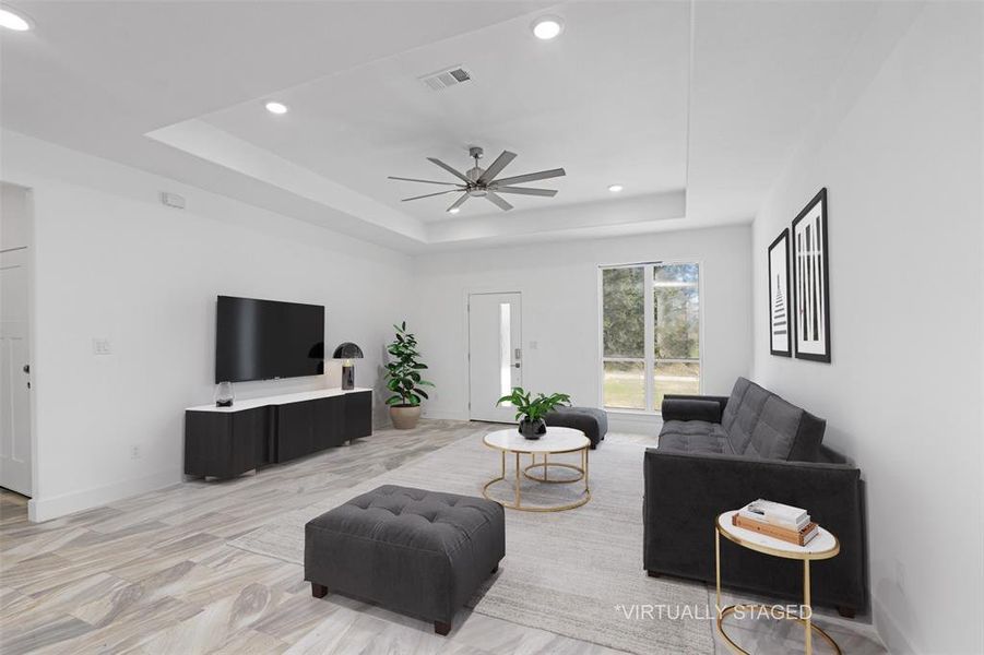 Living room featuring a tray ceiling, ceiling fan, and light hardwood / wood-style flooring