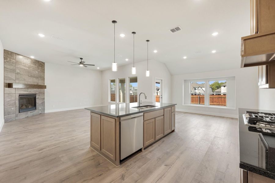 Open kitchen with center island, pendant lights, and stone fireplace in adjoining living room
