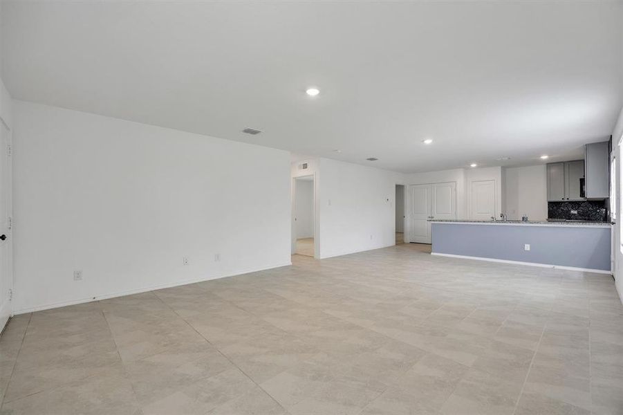 Spacious open-concept living area featuring light-toned tile flooring, recessed lighting, and a kitchen bar with a dark countertop