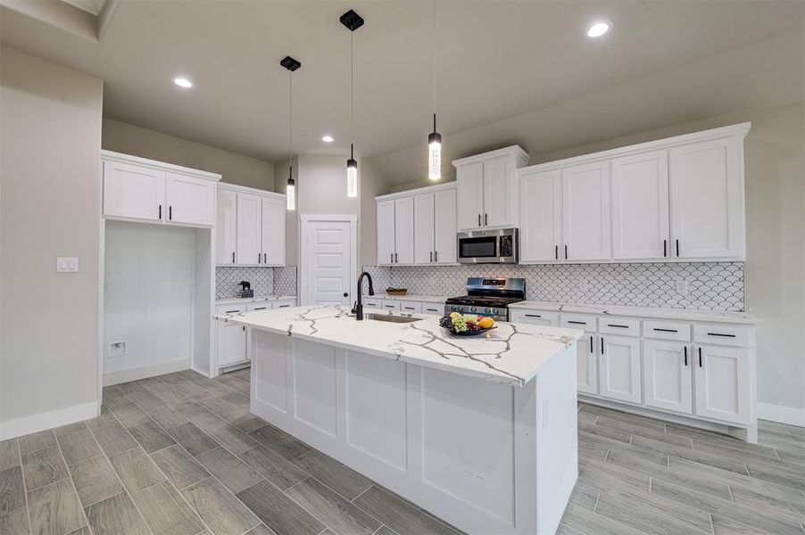 Kitchen featuring appliances with stainless steel finishes, pendant lighting, white cabinetry, an island with sink, and light stone countertops