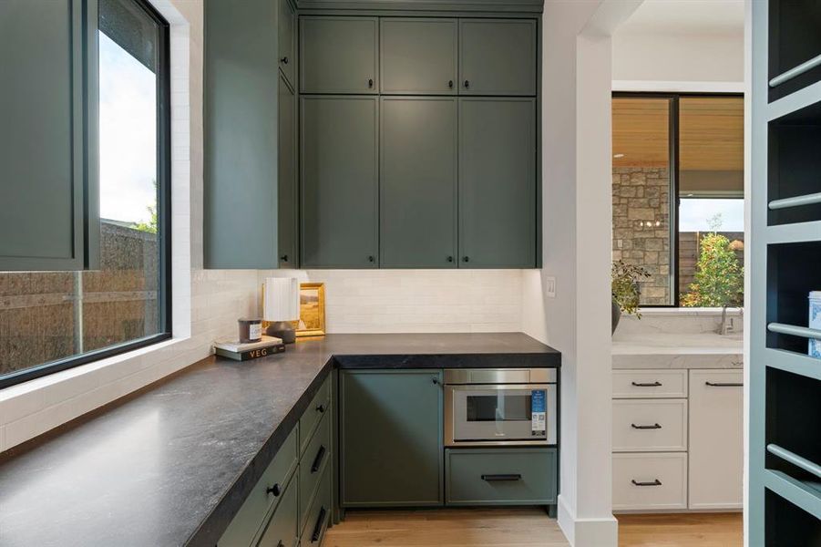 Kitchen with green cabinets, dark countertops, light wood-style floors, and stainless steel microwave Kitchen with green cabinets, dark countertops, light wood-style floors, and stainless steel microwave