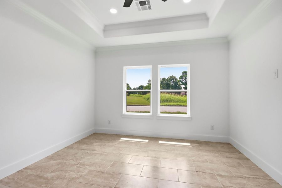Bright and airy primary bedroom with large windows overlooking lush greenery, featuring elegant flooring and a stylish tray ceiling with recessed lighting.