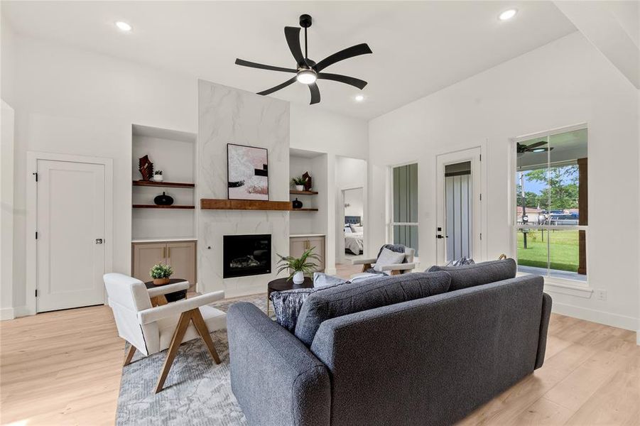 Living area featuring ceiling fan, light wood-style flooring, built in shelves, recessed lighting, and a fireplace Living area featuring ceiling fan, light wood-style flooring, built in shelves, recessed lighting, and a fireplace