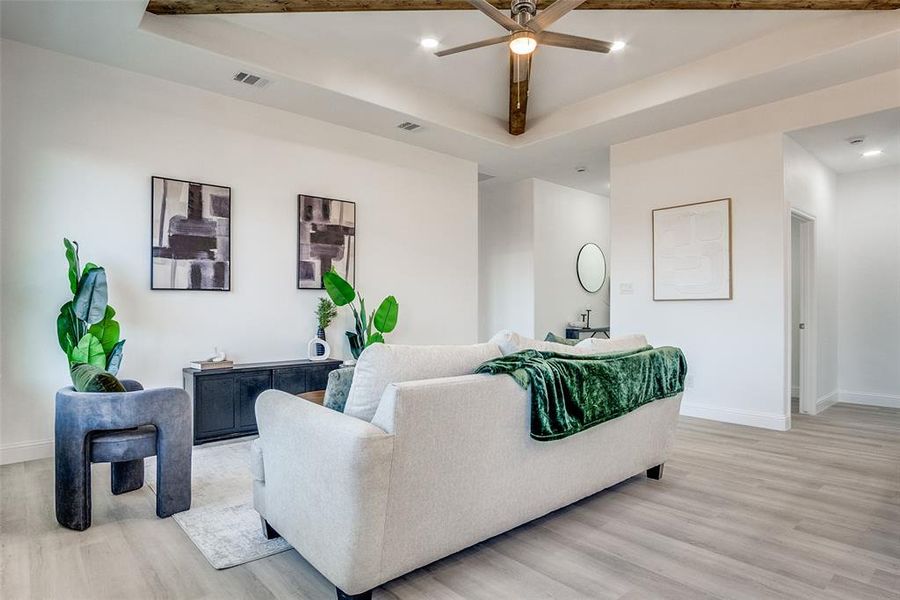 Living room with light wood-style flooring, a ceiling fan, recessed lighting, and a raised ceiling Living room with light wood-style flooring, a ceiling fan, recessed lighting, and a raised ceiling