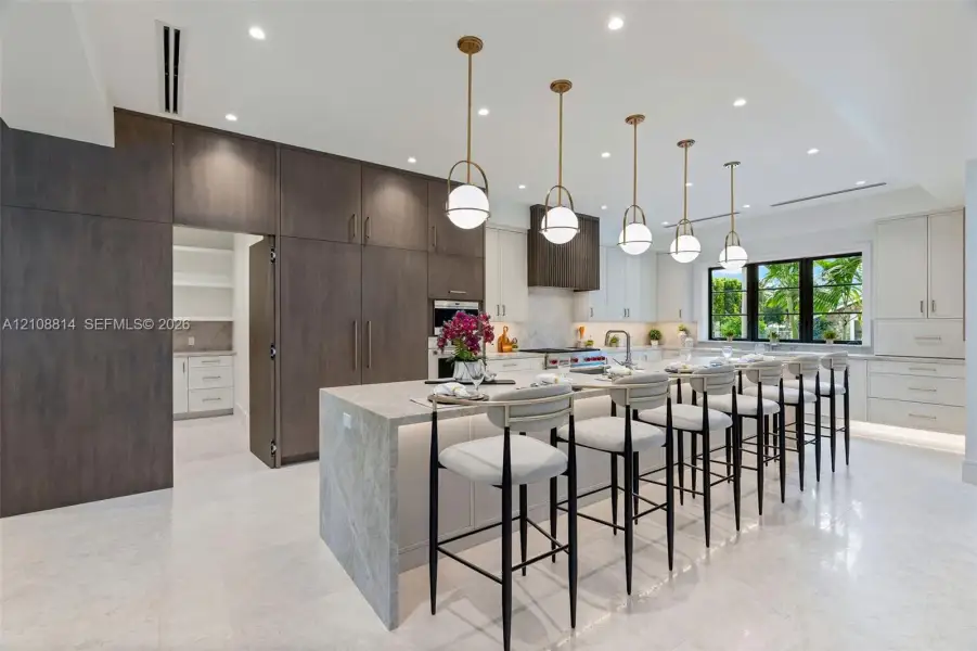 Kitchen featuring a waterfall-edge center island, two-tone custom cabinetry, stone-style countertops, professional-grade stainless steel appliances, and tiered globe pendant lighting Kitchen featuring a waterfall-edge center island, two-tone custom cabinetry, stone-style countertops, professional-grade stainless steel appliances, and tiered globe pendant lighting