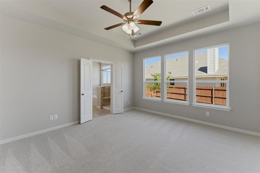 Empty room with light carpet, a raised ceiling, and ceiling fan