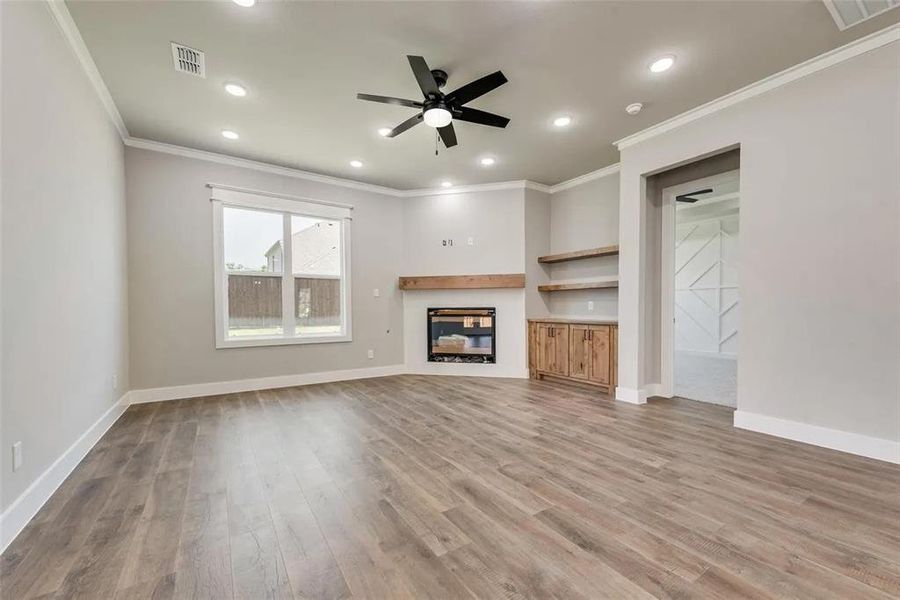 Unfurnished living room with a ceiling fan, a glass covered fireplace, crown molding, light wood-style floors, and recessed lighting